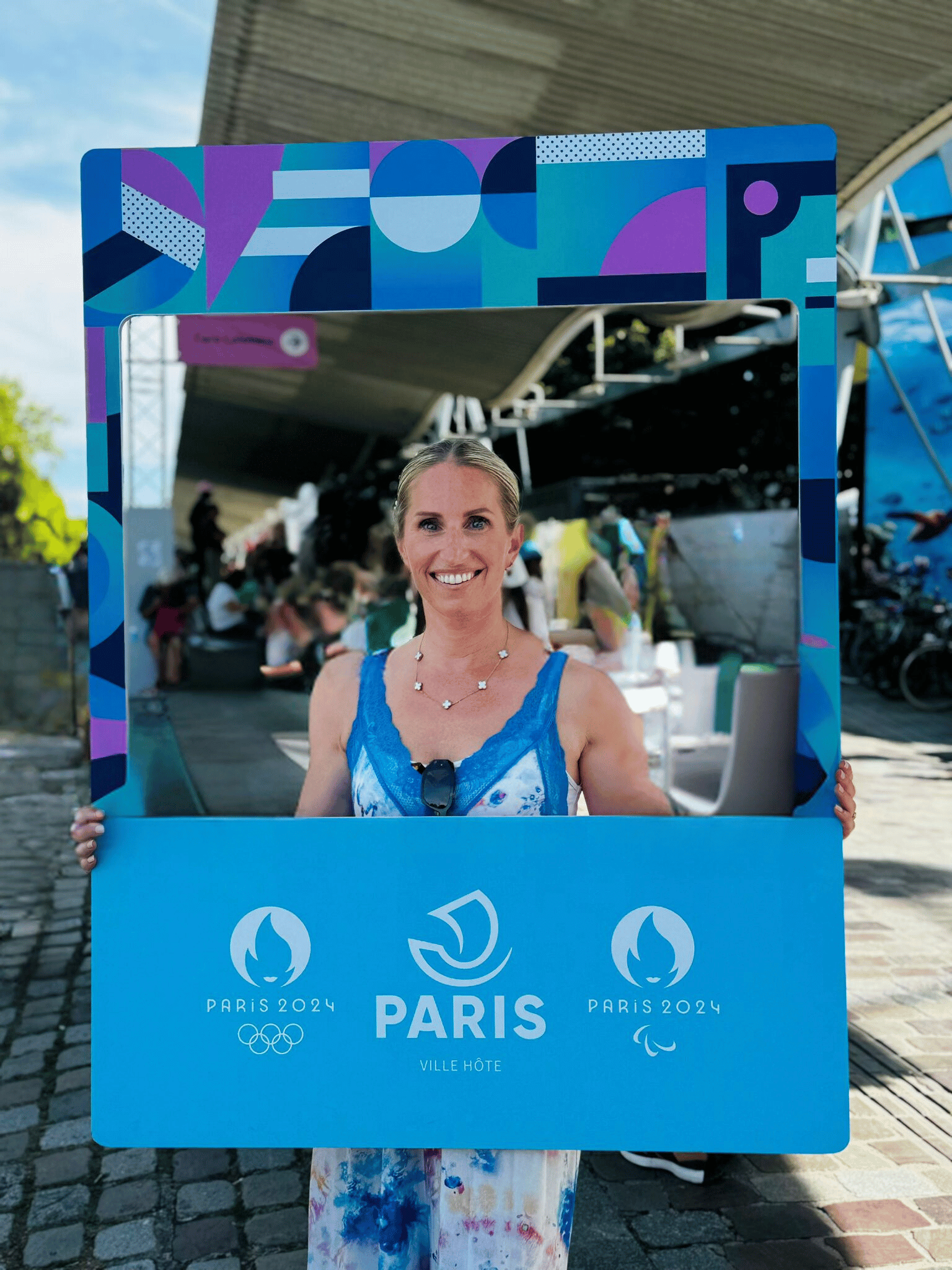 Jennifer de chez Transbeauté tient un cadre promotionnel de Paris 2024 lors d'un événement lié aux Jeux Olympiques et Paralympiques. La visibilité et l'inclusion des personnes LGBT aux Jeux de Paris 2024 soulignent l'engagement pour des Jeux ouverts, respectueux de la diversité et des droits humains.