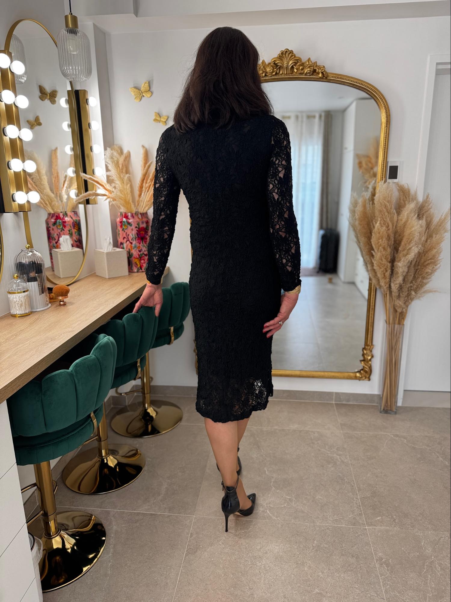 Caroline, travesti en robe noire, se regarde dans un grand miroir après une séance de maquillage et de féminisation chez Transbeauté.