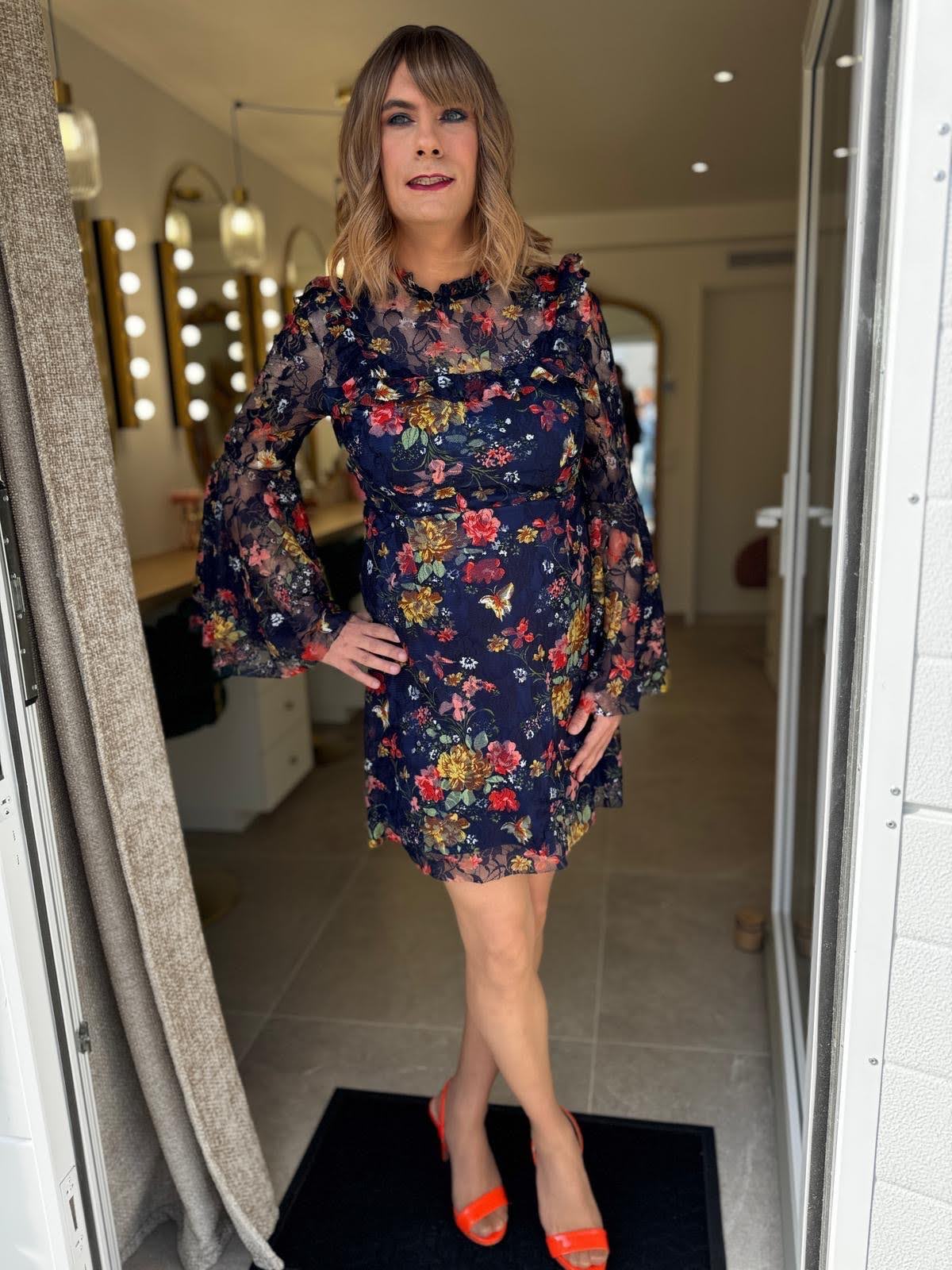 Tina, bigenre, pose en robe fleurie et escarpins après une séance maquillage et féminisation chez Transbeauté près de Paris.