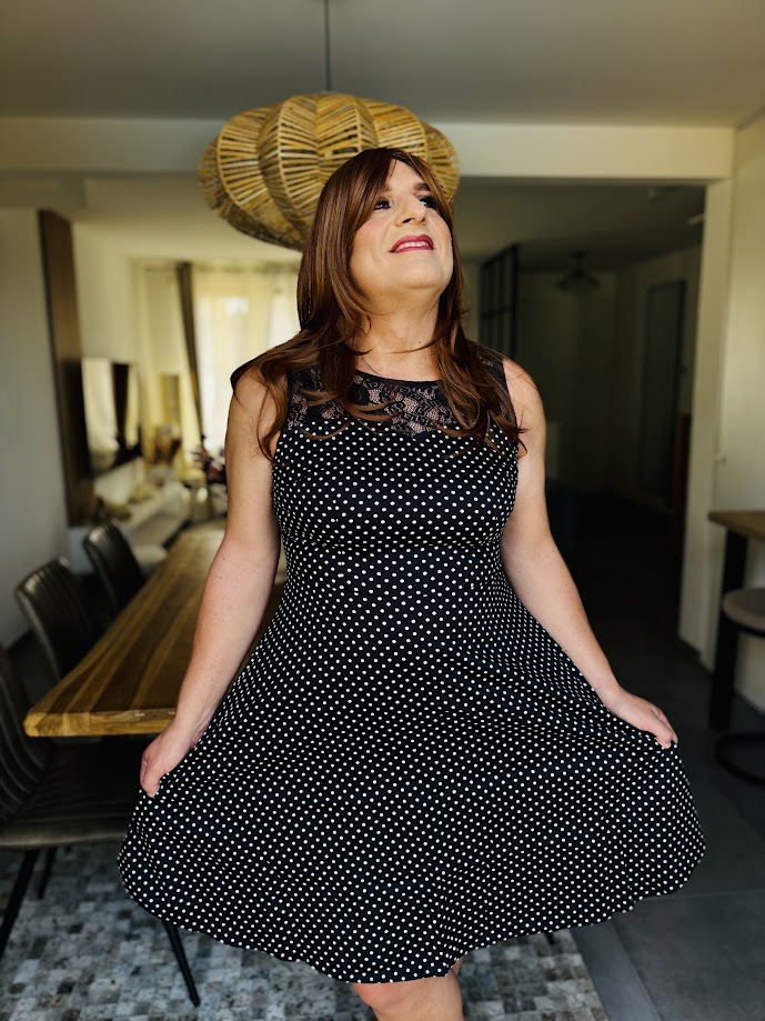 Sandy pose dans une robe évasée à pois blancs, les cheveux bruns sur les épaules et le sourire aux lèvres. Cette photo illustre sa journée chez Transbeauté, partagée avec son épouse entre maquillage, essayages et shopping. Une expérience qu’elle raconte avec ces mots : « Grâce aux photos, je me suis dit : “Waouh, je suis belle !” »